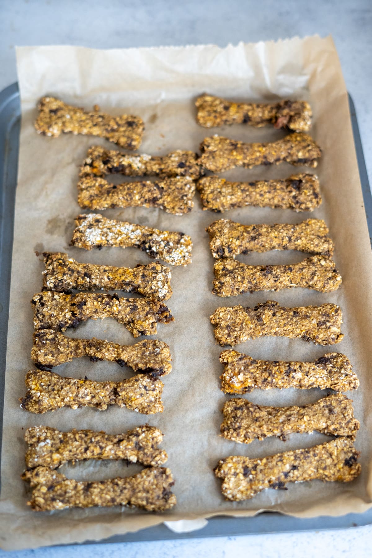 Lamb and sweet potato dog treats shaped like bones arranged in rows on a baking tray lined with greaseproof paper.