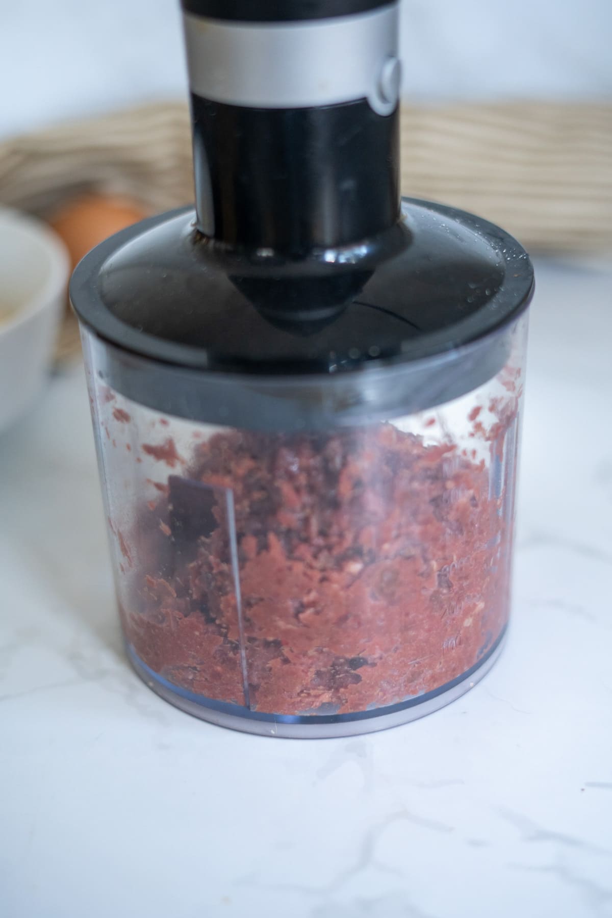Immersion blender chopper attachment filled with finely minced dark red ingredients for lamb and sweet potato dog treats.