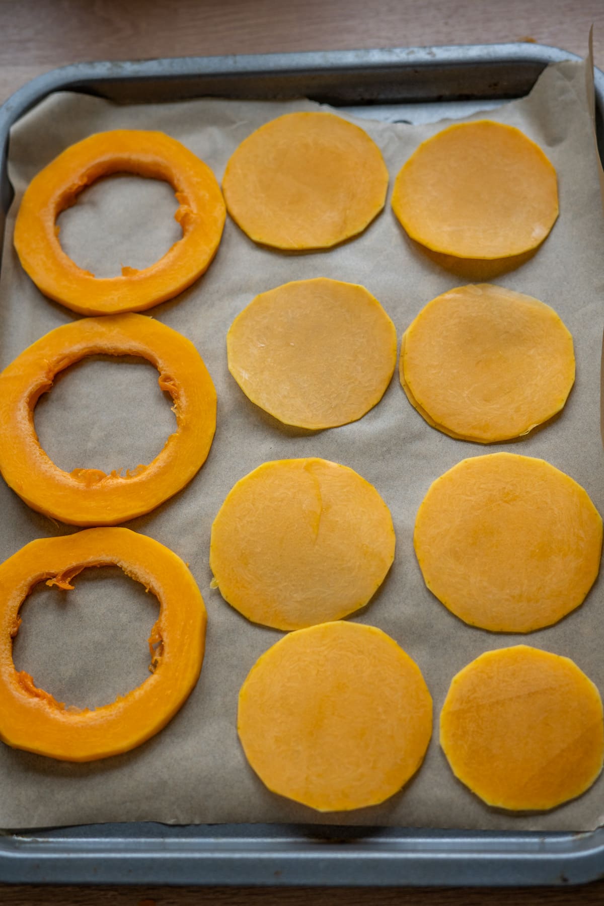 Slices of butternut squash crisps for dogs arranged on a baking tray lined with baking paper.