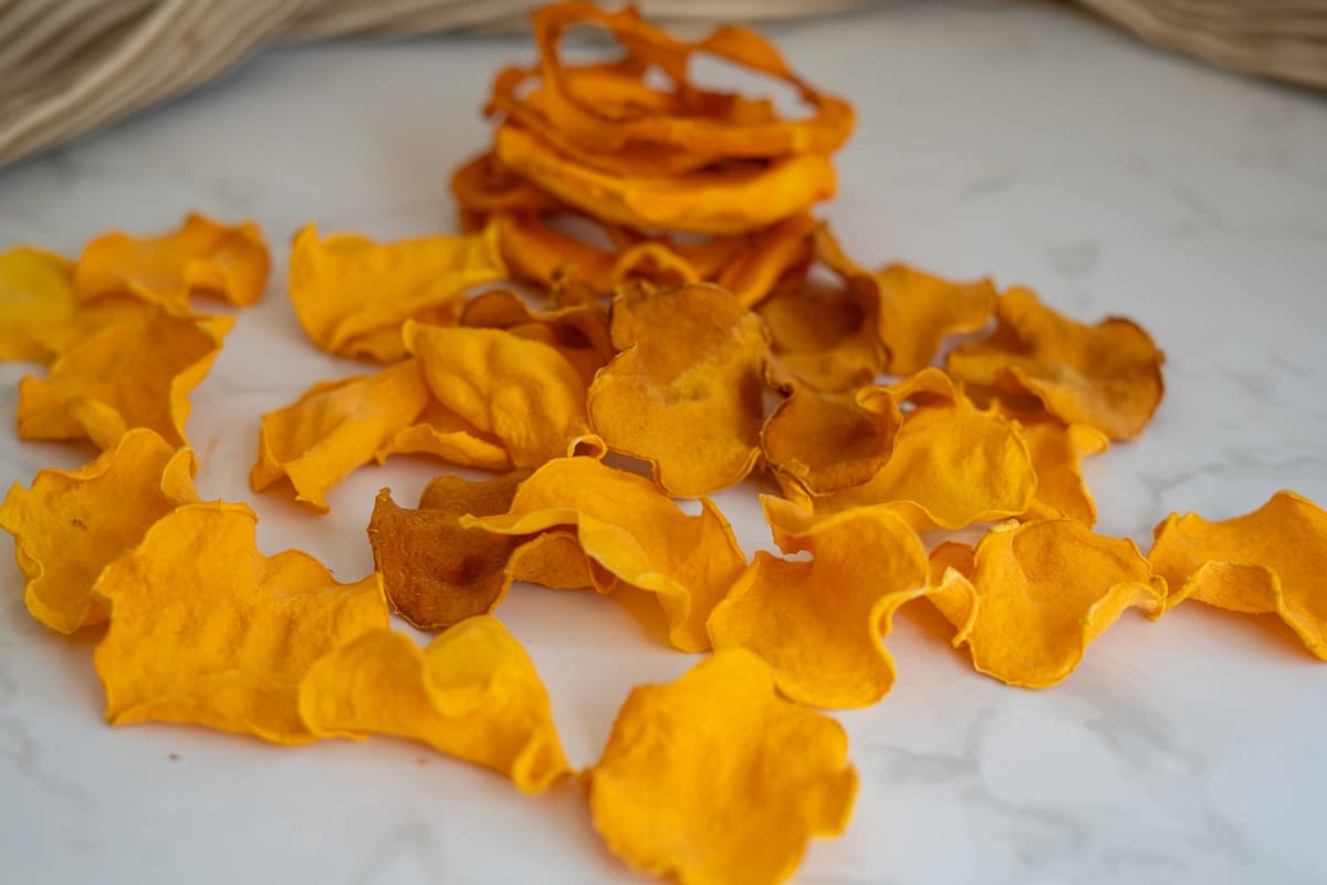 Dried butternut squash crisps for dogs scattered on a white surface with a small stack in the background.