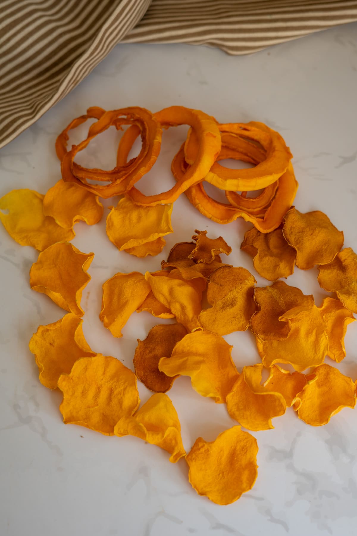 A pile of thin, dried butternut squash crisps for dogs on a white surface.
