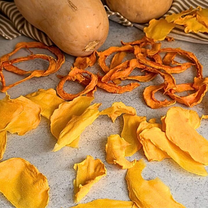 Two whole butternut squashes sitting next to a pile of dehydrated squash rings and dried mango slices.