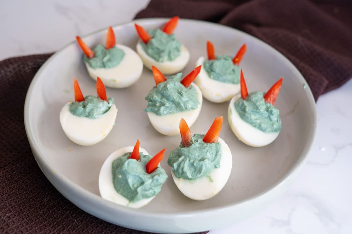 Devilled eggs topped with green filling and red pepper slices arranged on a plate.