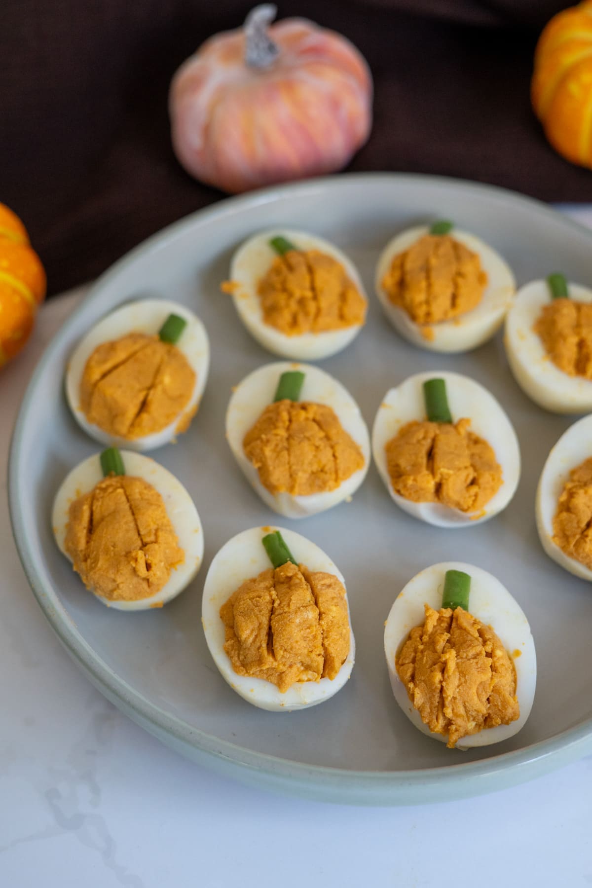 Devilled eggs decorated to look like pumpkin devilled eggs for dogs, topped with small pieces of chives as stems, arranged on a grey plate.