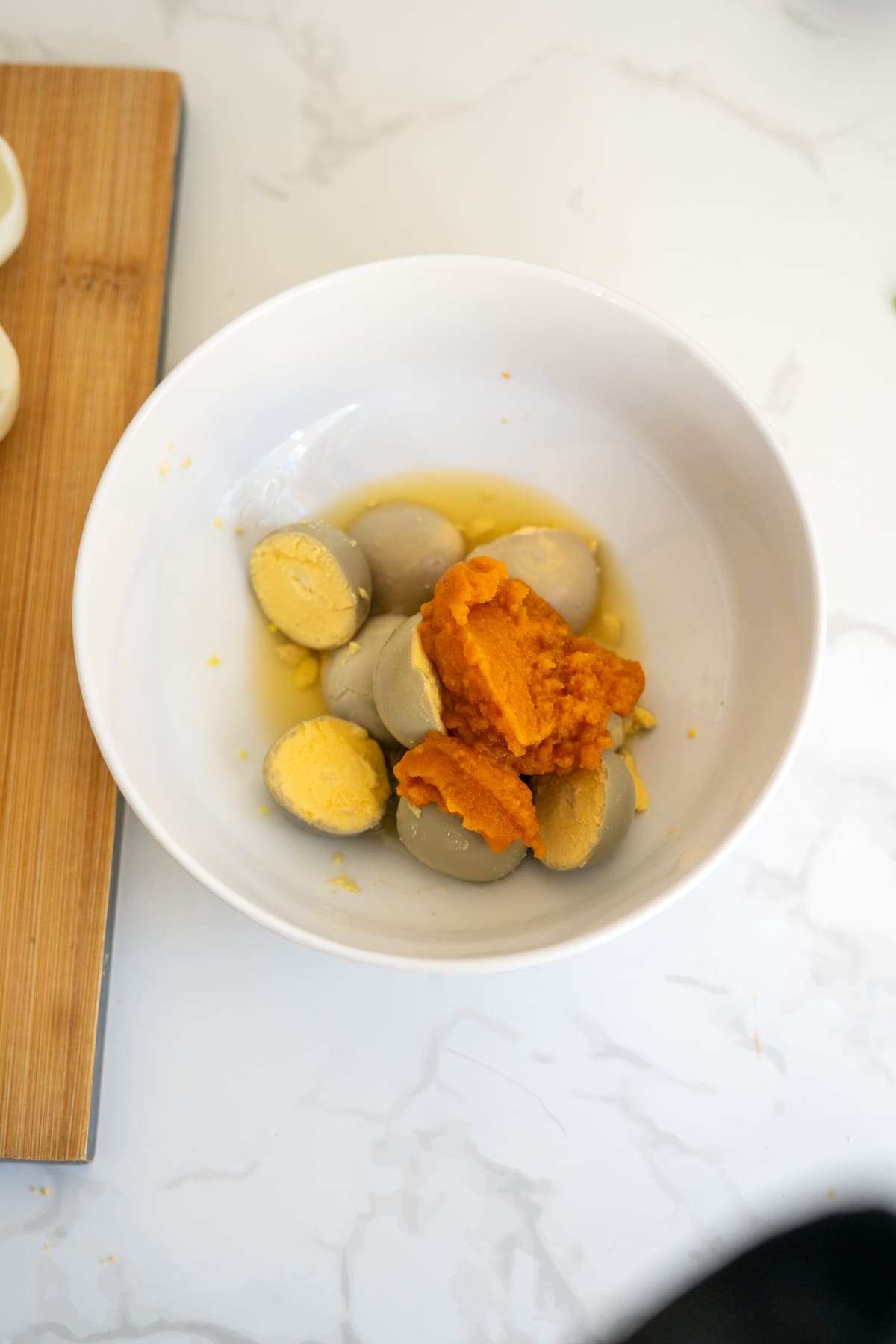 A white bowl containing peeled hard-boiled eggs and a mound of orange purée, prepared as pumpkin devilled eggs for dogs.