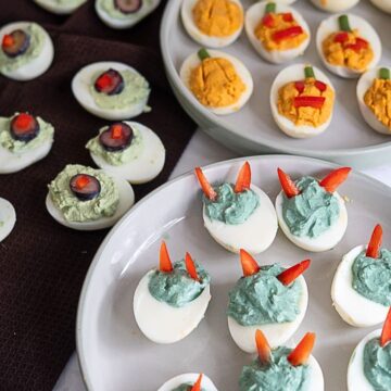 Devilled eggs decorated to look like pumpkins and monsters, with some topped with olive slices, arranged on plates.