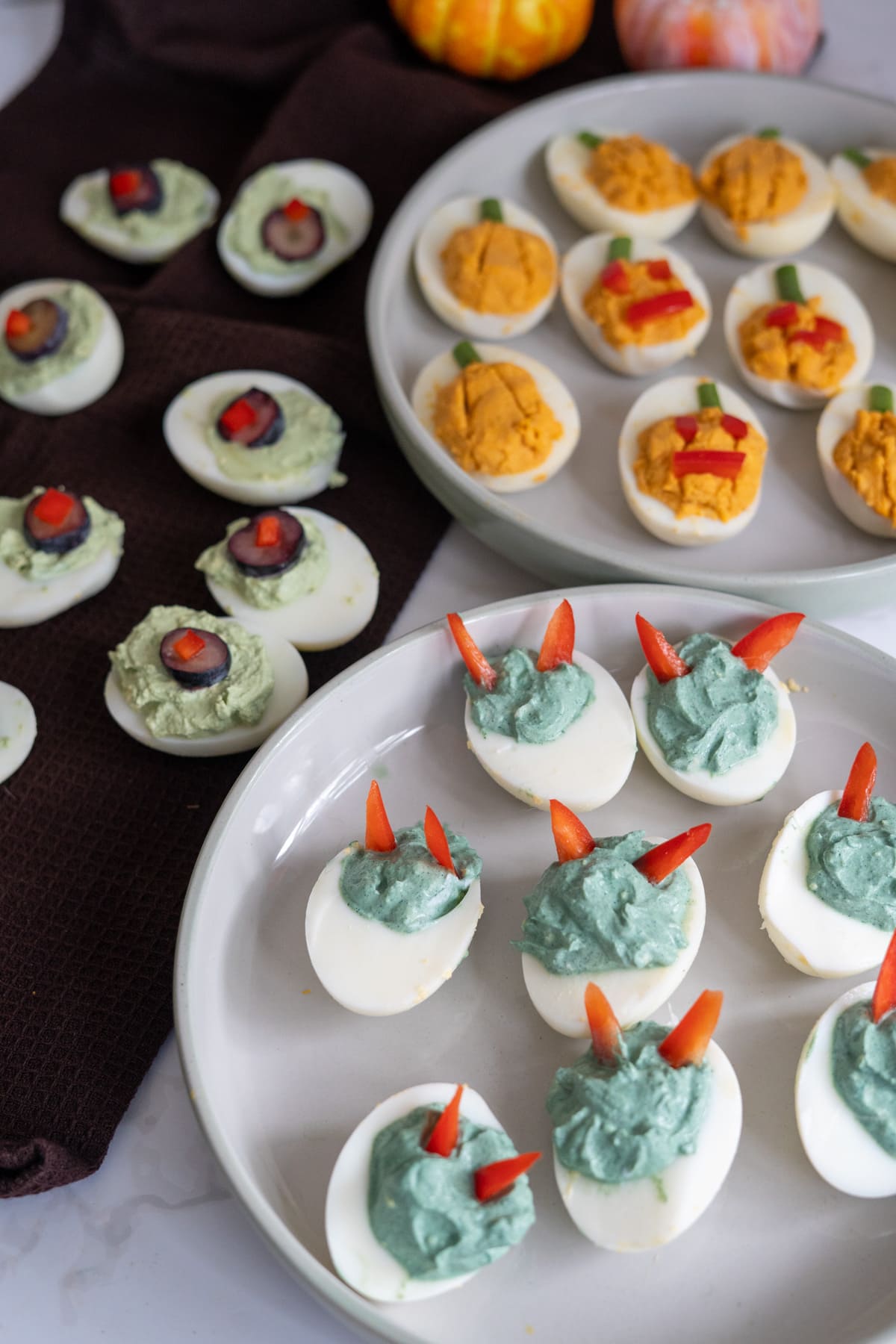 Halloween devilled eggs for dogs decorated as treats, including pumpkin-shaped eggs with pepper stems and blue-tinted monster eggs with red pepper horns.