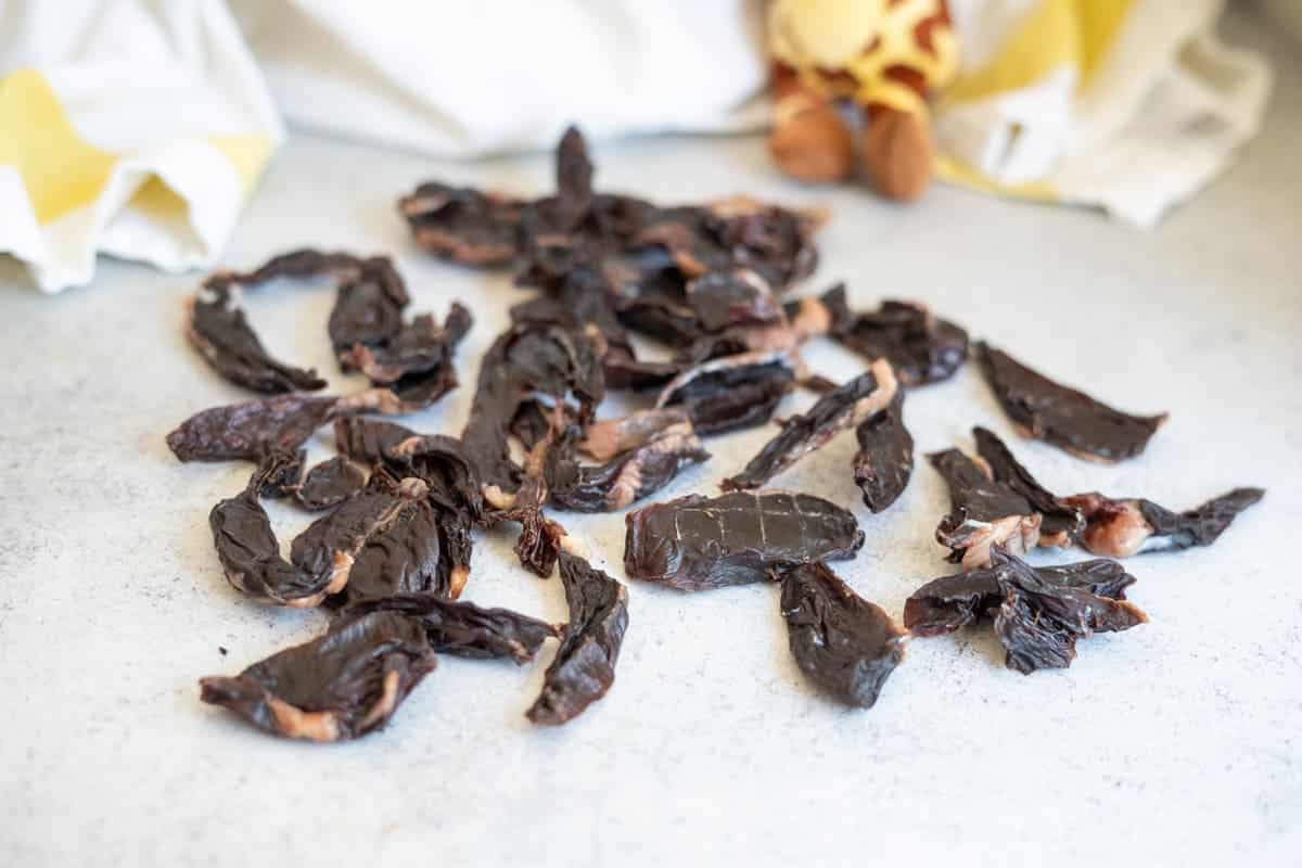 A pile of dark, dried lamb heart dog treats on a light-coloured surface.