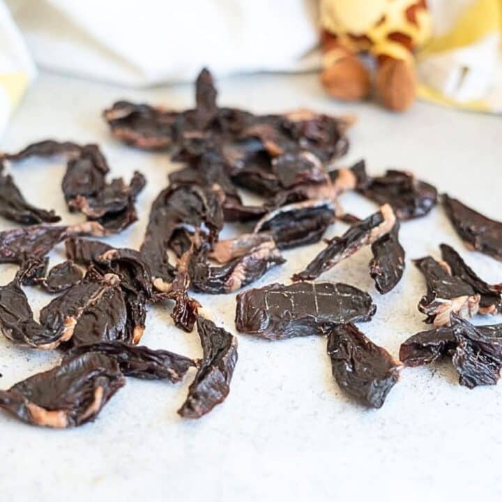 A pile of dark, dried meat treats on a white surface.