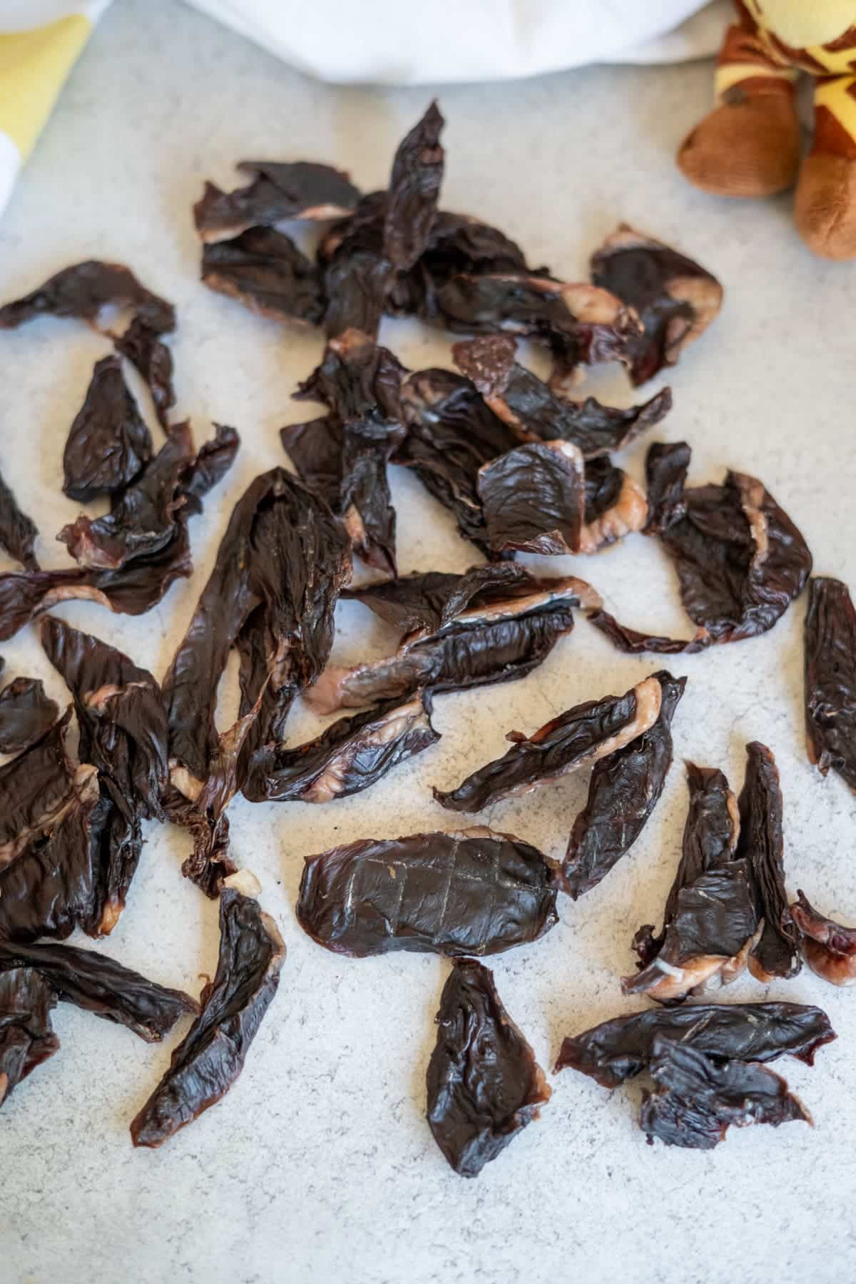 Scattered pieces of dark, dried lamb heart jerky on a light surface.