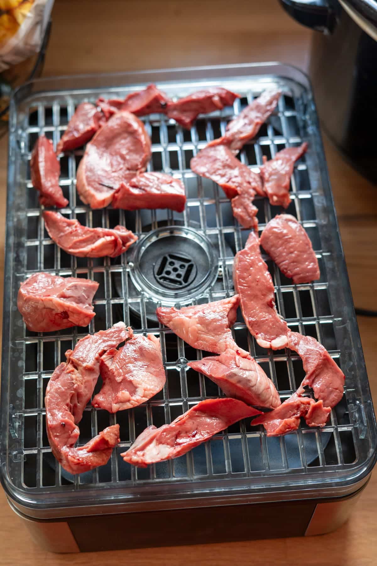 Raw pieces of lamb heart arranged on a plastic food dehydrator tray to make dog treats.