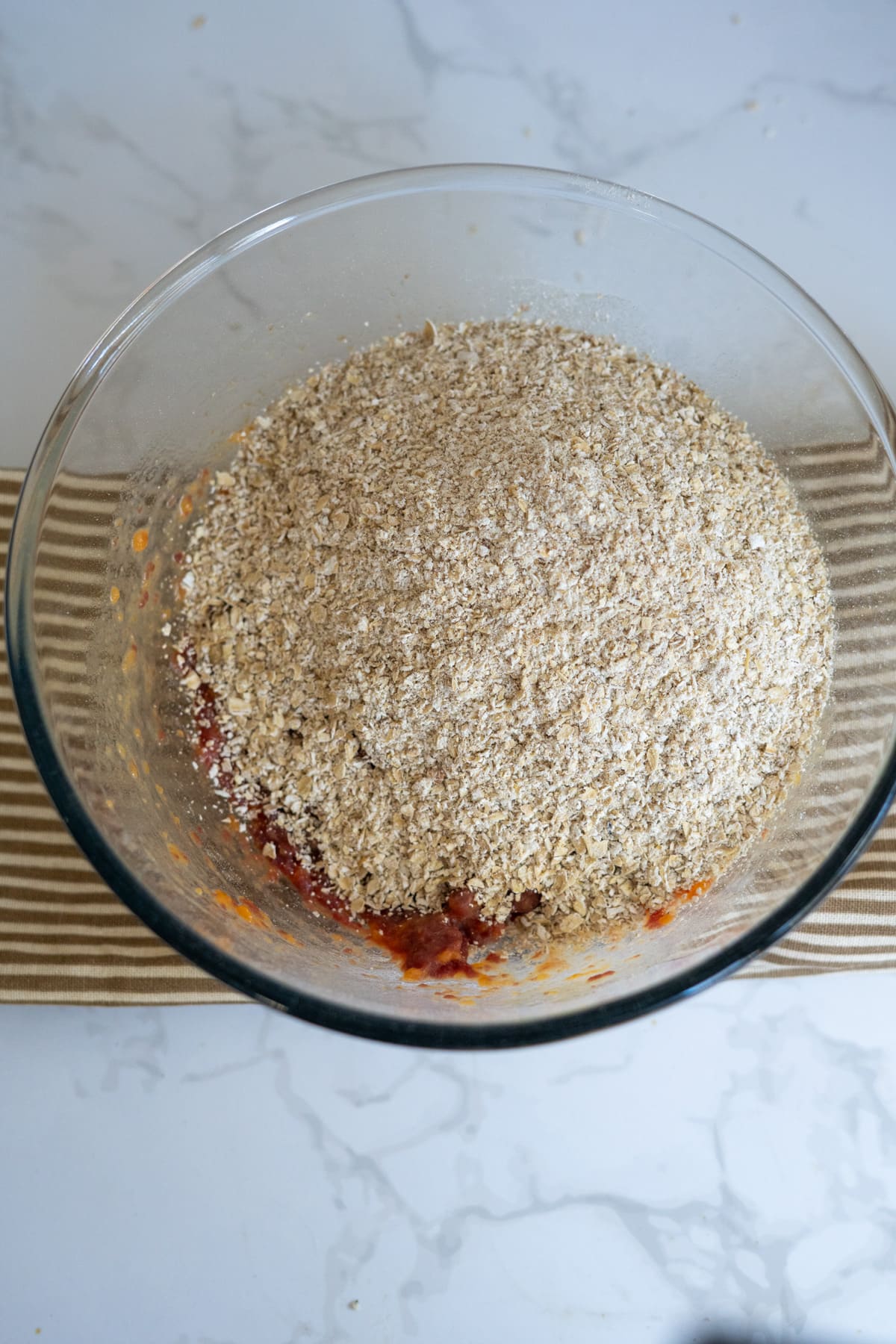 A glass bowl containing a base of lamb and sweet potato mixture topped with a pile of dry oats.
