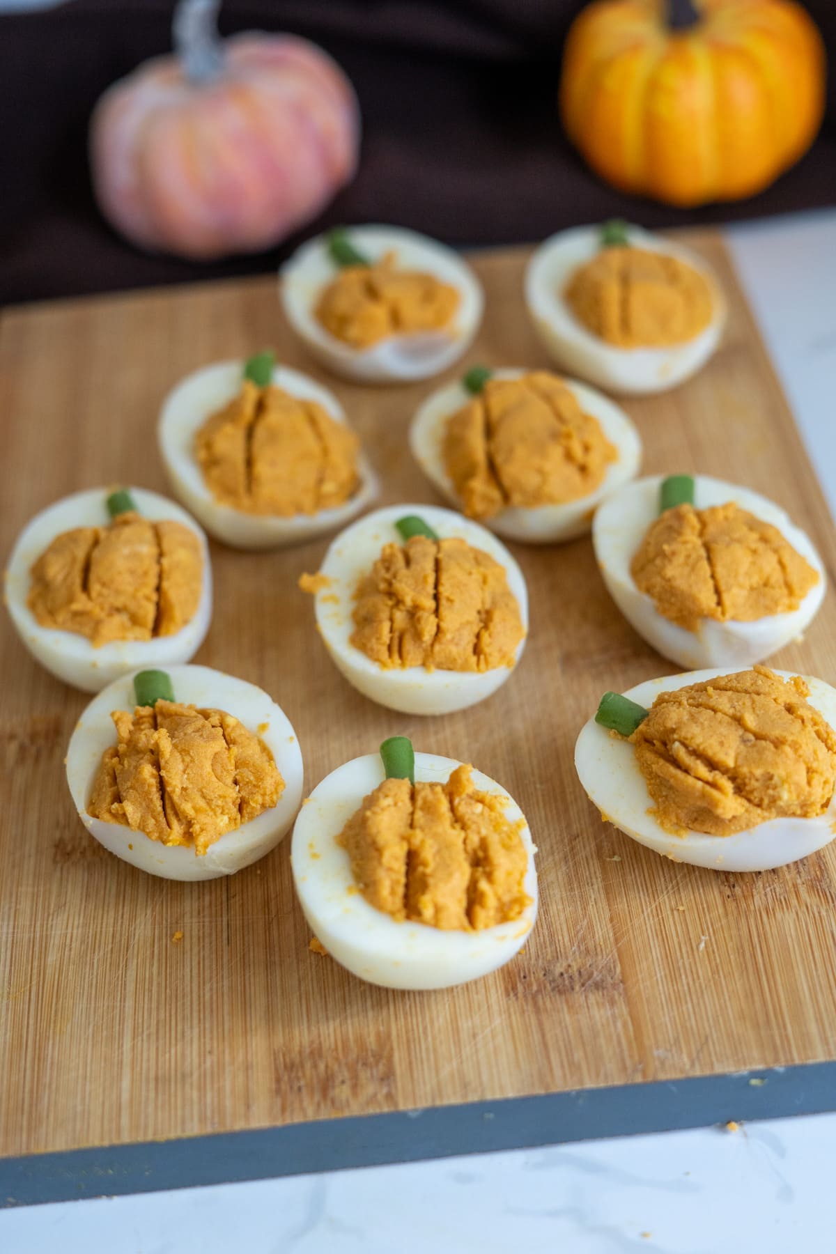 Pumpkin devilled eggs for dogs arranged on a wooden board, with the yolk filling shaped like pumpkins and topped with small green stems.