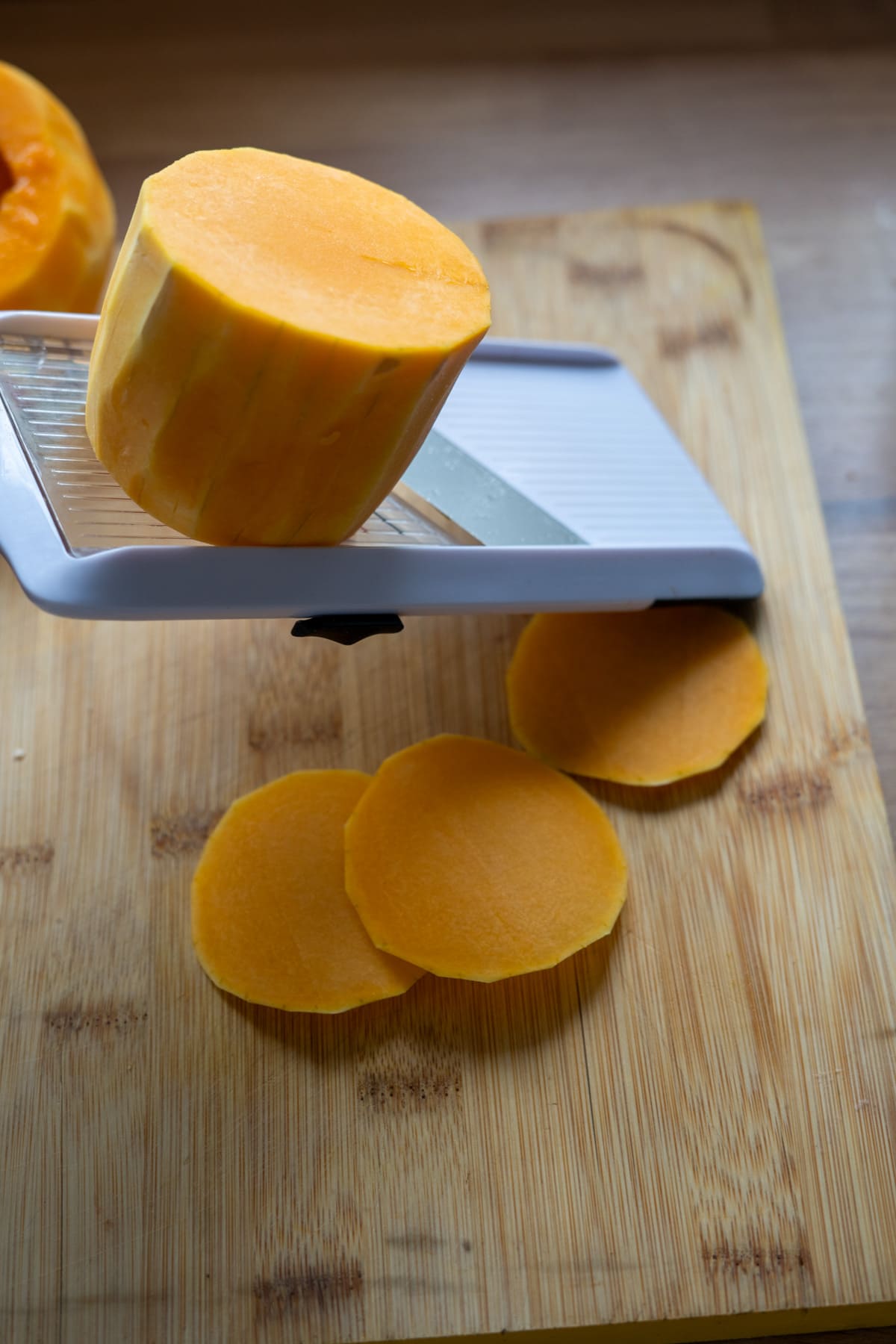 A peeled butternut squash being sliced on a mandoline over a wooden chopping board to make butternut squash crisps for dogs.